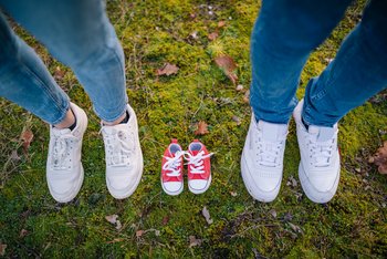 Rote Kinderschuhe zwischen den Eltern mit weißen Sneakern auf Moos im Wald bei Herbst